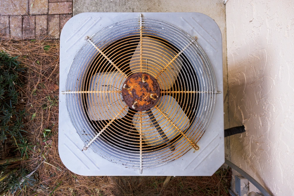 Top-down view of an old outdoor air conditioner unit featuring a rusted metal fan grate.